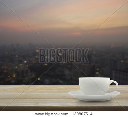 White cup on wooden over blurred aerial view of cityscape on warm light sundown