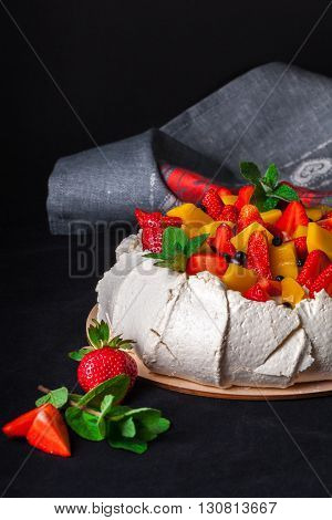 Snow-white meringue Pavlova Cake with fresh strawberries, slices of mango, blueberries and fresh mint on a dark background. Pavlova desert. Whipped cream cheese and mascarpone with berries and fruits