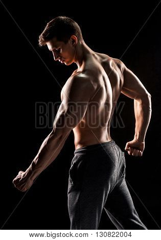 Strong bodybuilder man posing with perfect abs, houlders, biceps, triceps and chest on black background.