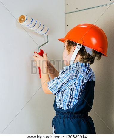 Four year old boy in protective helmet construction painstakingly paints the wall roller