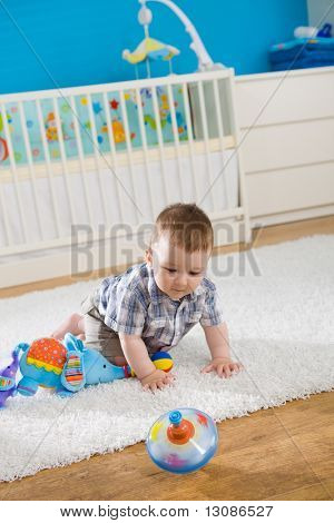Baby boy ( 1 year old ) sitting on floor at home and playing with whirligig.