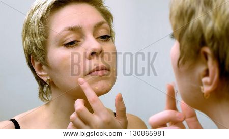 Beautiful young woman applies concealer foundation cream make up in front of mirror. Beauty and makeup concept.