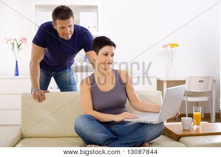 Coppia utilizzando computer portatile a casa insieme, davanti allo schermo, sorridente.