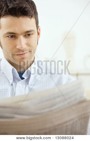 自宅で新聞を読んで、ハンサムな若い男。