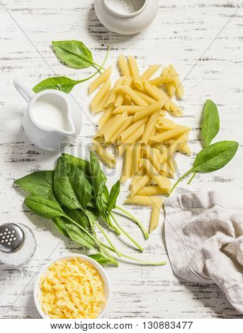 Raw ingredients for making pasta with spinach cream sauce - penne pasta fresh spinach cream cheese and spices on a light wooden background