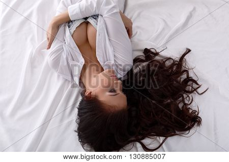 Erotica. Top view of long-haired brunette lying in bed