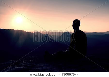 Sportsmann Hiker In Black Sportswear Sit On Mountain Top And Take A Rest. Tourist  Watch Down To Mor
