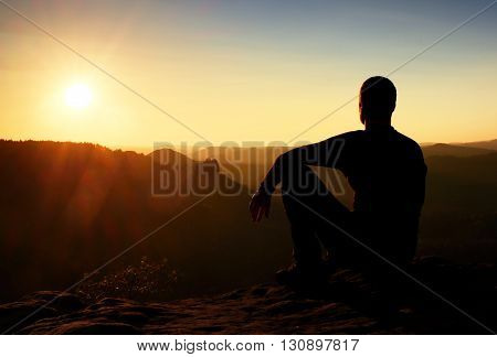 Sportsmann Hiker In Black Sportswear Sit On Mountain Top And Take A Rest. Tourist  Watch Down To Mor