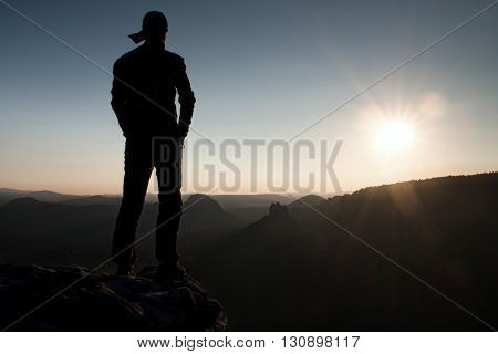 Hiker In Long Cap On Rock Empire And Watching To Sun. Beautiful Moment The Miracle Of Nature