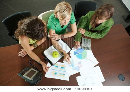 Unge erhvervskvinder sidder ved bord i mødelokalet, diskuterer finacial diagrammer. Overhead skud.