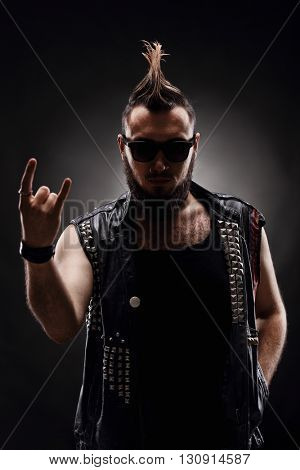 Vertical shot of a punk rocker making a hardcore hand gesture on dark background