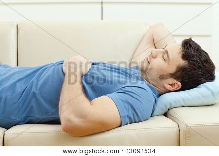 Giovane uomo bello dormire sul divano a casa, vista laterale.