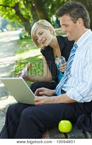 Giovani imprenditori seduto sulla panchina nel parco avendo luch e guardando il computer portatile.
