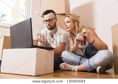 Young couple in love sitting on the floor of their new apartment planning redecoration and drinking juice