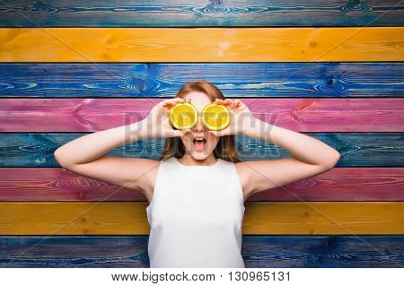 Young girl holds half of a juicy orange. Surprised face. Young girl on a colorful striped background. Fruit fashion girl. Full face. Bright juicy picture