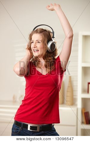 Happy teen girl singing and dancing with headphones at home smiling.