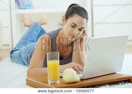 Happy Woman auf Boden zu Hause liegen und arbeiten auf Laptop-Computer, lächelnd.