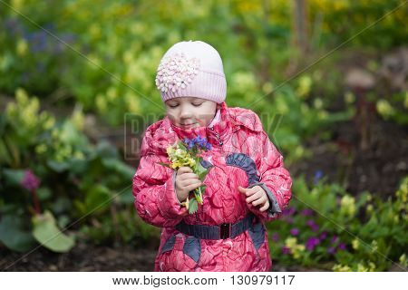Little girl holding yellow flower bouquet in spring garden