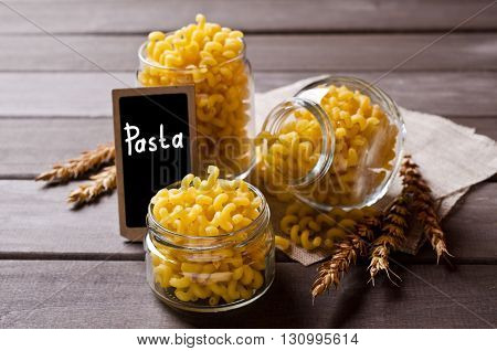 Dried pasta cavatappi in the glass on a wooden background. Selective focus.