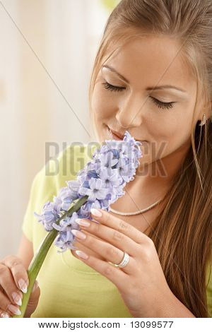Beautiful woman smelling flowers with closed eyes, holding flower with two hands.