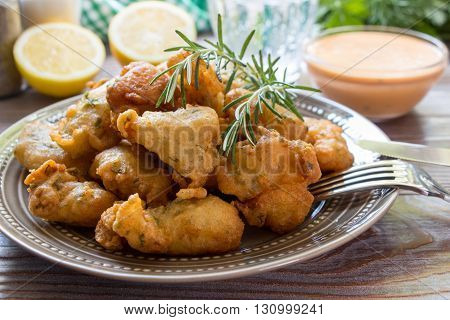 In foreground shrimps in crispy dough on a plate with rosemary, cutlery, in background glass of water, lemon, herbs, salt, pepper, bowl with sauce. Shrimps in pastry for lunch. Horizontal. Close.