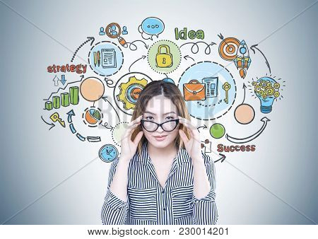 Attractive And Serious Asian Businesswoman Wearing A Striped Shirt Is Touching Her Glasses And Looki