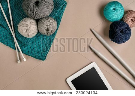 Grey And Turquoise Knitting Wool, Knitting Needles And A Tablet With A Black Screen On Beige Backgro