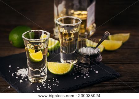 Gold Tequila Shot With Lime And Sea Salt On Black Table.