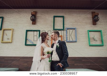 Bride And Groom Standing At Wall With Frames