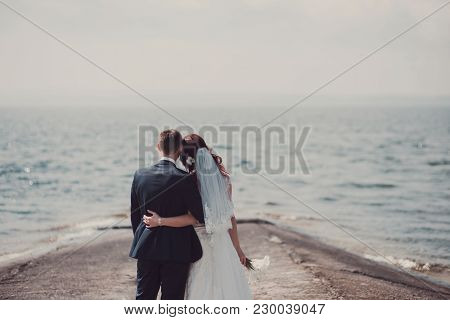 Wedding Couple Kissing And Hugging On Rocks Near Blue Sea