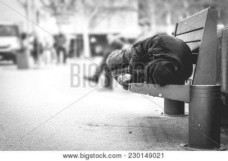 Poor Homeless Man Or Refugee Sleeping On The Wooden Bench On The Urban Street In The City, Social Do