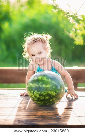 A Little Girl In A Green Sarafan Smiles In Summer Against A Background Of Green Young Grass. Child A