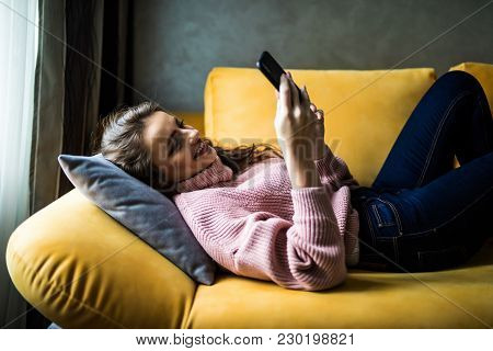 Close Up Of A Relaxed Girl Using A Smart Phone Lying On A Sofa In The Living Room At Home