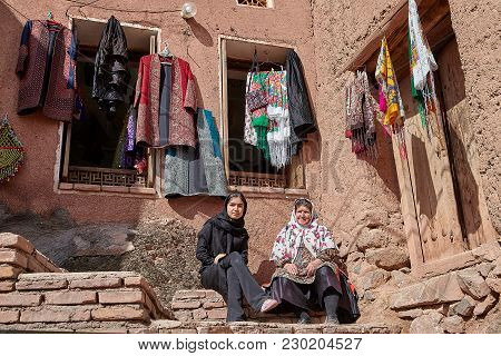 Abyaneh, Iran - April 26, 2017: Two Iranian Women In Hijabs Sit In Traditional Countryside In The Mo