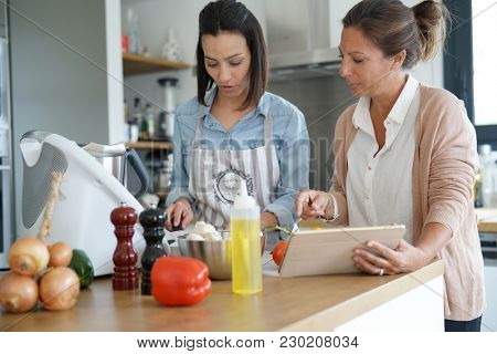 Friends cooking together with kitchen robot and tablet