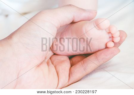Newborn Baby Feet On Mother Hands On Bed
