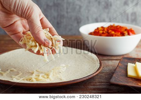 Woman Sprinkles With Cheese Tortilla For Cooking Mexican Quesadilla. The Concept Of National Cuisine