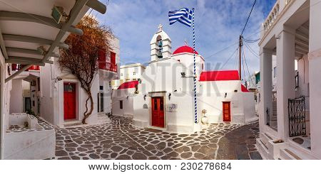 Agia Kyriaki Church, Typical Greek Church Building And Large Waving Greek Flag Against The Blue Sky 