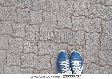 Pair Of Blue Booted Feet With White Laces On Patterned Paving  Stones.  Feet Are By The Edge With Sp