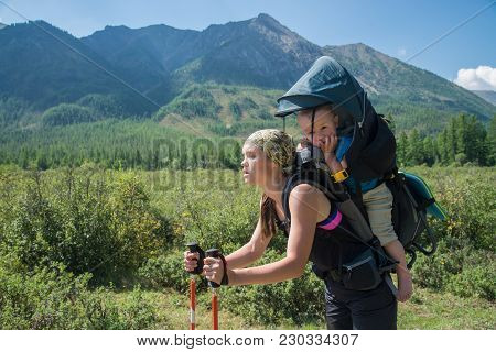 Tired Woman Hiker Trekking In Mountains With Child In Backpack, Stopped For Rest. Mother With Baby B