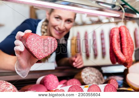 Sales woman in meat shop showing a heart shaped sausage to customer