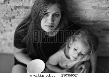 Homeless poor woman with little daughter holding empty bowl and asking alms near brick wall