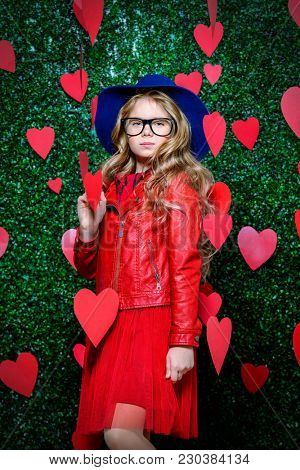 Happy pre-teen girl poses surrounded by little hearts over lawny background. First love. Valentine's Day.