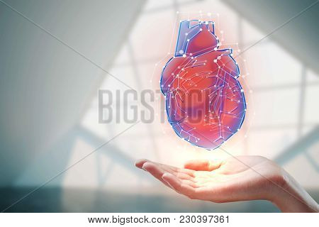 Female Hand Holding Abstract Heart Hologram On Blurry Interior Background. Medicine, Cardiology And 