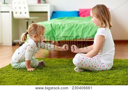 childhood, leisure and family concept - happy little girls playing rock-paper-scissors game or making fist bump at home