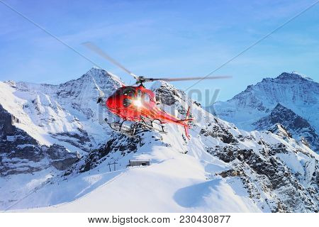 Red Helicopter Flying In Swiss Alps Mountain Mannlichen In Winter, Switzerland