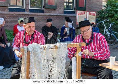 Urk, The Netherlands - September 02, 2017: Two Men In Traditional Clothing Mending Fishing Nets At A