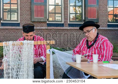Urk, The Netherlands - September 02, 2017: Two Men In Traditional Clothing Mending Fishing Nets At A