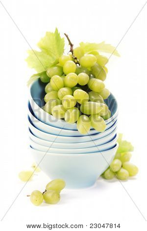 Pila di ciotole e uva verde fresca sopra bianco