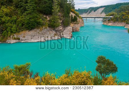 Bridge over river Rakaia with a view at  turquoise river and blooming yellow gorse